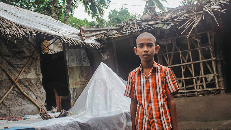 Sourob uit Bangladesh staat voor zijn huis, dat is verwoest door een cycloon.