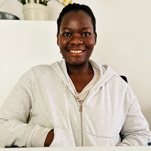 Joyce uit Uganda zit met haar handen in haar zakken aan tafel.