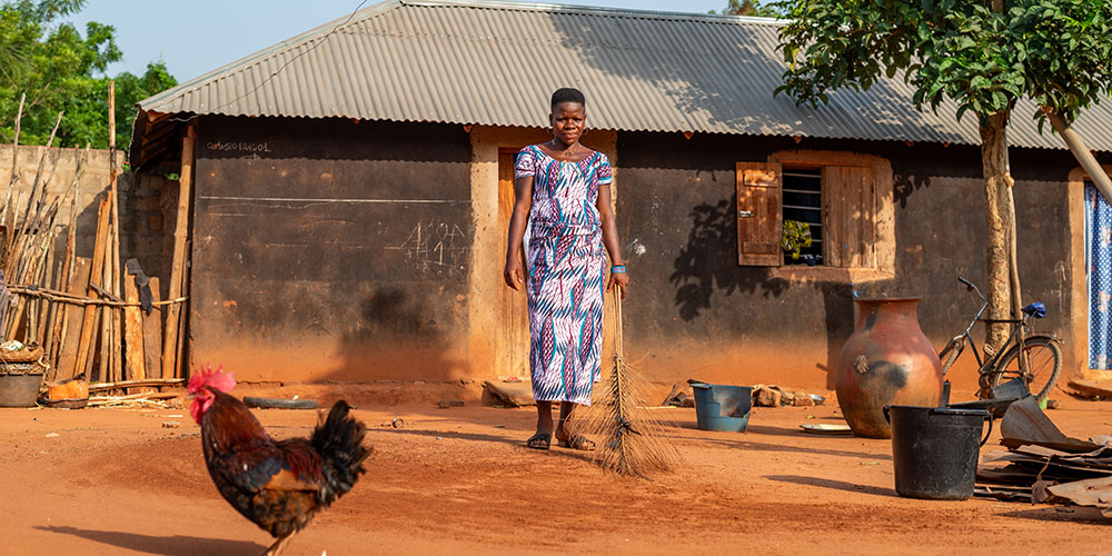 Davi uit Togo staat met een bezem in haar hand voor haar huis.